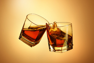 Image showing Two whiskey glasses clinking together on brown