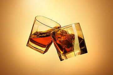 Image showing Two whiskey glasses clinking together on brown