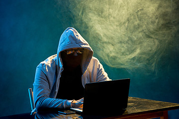 Image showing Hooded computer hacker stealing information with laptop