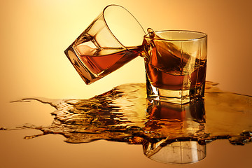 Image showing Two whiskey glasses clinking together on brown