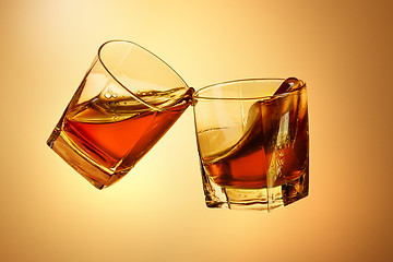 Image showing Two whiskey glasses clinking together on brown