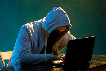 Image showing Hooded computer hacker stealing information with laptop