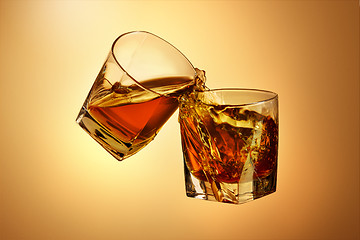 Image showing Two whiskey glasses clinking together on brown