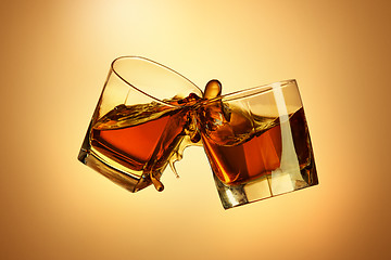 Image showing Two whiskey glasses clinking together on brown