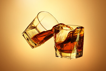 Image showing Two whiskey glasses clinking together on brown