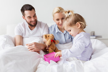 Image showing happy family with gift box in bed at home