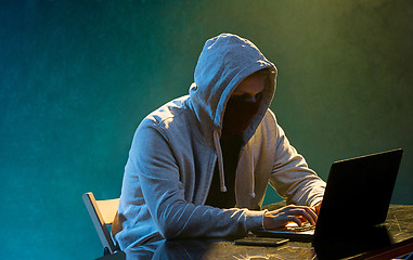 Image showing Hooded computer hacker stealing information with laptop