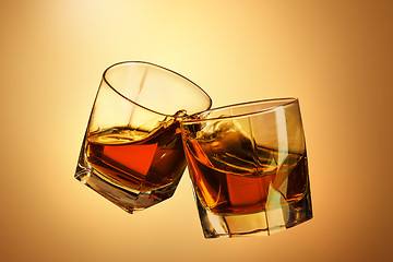 Image showing Two whiskey glasses clinking together on brown