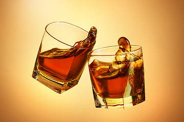 Image showing Two whiskey glasses clinking together on brown