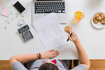 Image showing woman with tax report eating cookie at office