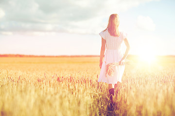 Image showing young woman with cereal spikelets walking on field