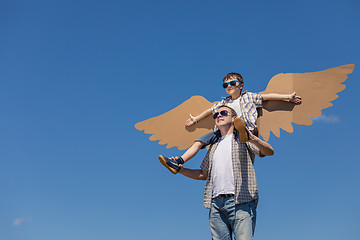 Image showing Father and son playing with cardboard toy wings in the park at t