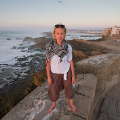 Image showing Female traveler standing barefooted on city fortress wall of Essaouira, Morocco.