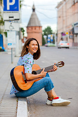 Image showing fun smiling woman with a guitar sits on the curb