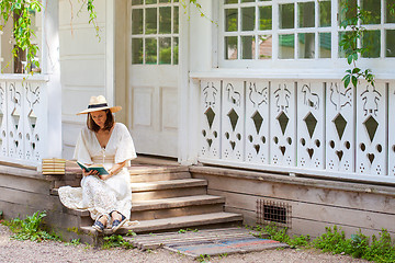 Image showing woman in a white dress and a straw hat reading a book on the por