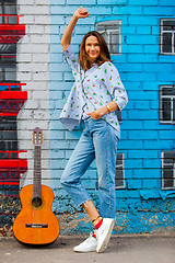 Image showing smiling woman in jeans stands near wall with graffiti next to gu