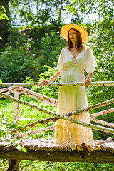 Image showing Beautiful woman in a white summer dress and a straw hat stands o