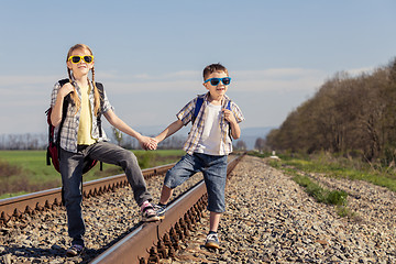 Image showing Happy brother and sister walking on the railway at the day time.