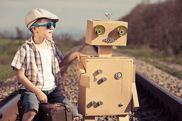 Image showing Happy little boy and robot walking with suitcase on the railway 