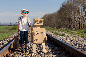 Image showing Happy little boy and robot walking with suitcase on the railway 