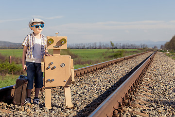 Image showing Happy little boy and robot walking with suitcase on the railway 