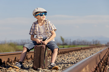 Image showing Happy little boy walking with suitcase on the railway at the day