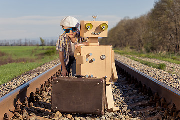 Image showing Happy little boy and robot walking with suitcase on the railway 