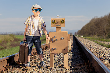 Image showing Happy little boy and robot walking with suitcase on the railway 