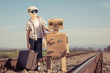 Image showing Happy little boy and robot walking with suitcase on the railway 