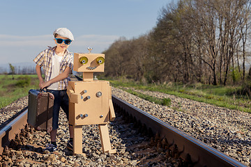 Image showing Happy little boy and robot walking with suitcase on the railway 