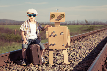 Image showing Happy little boy and robot walking with suitcase on the railway 