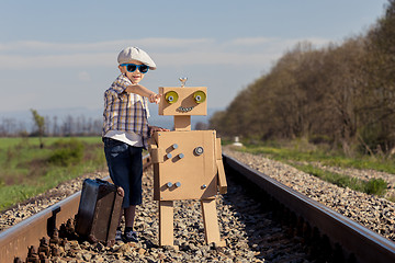 Image showing Happy little boy and robot walking with suitcase on the railway 