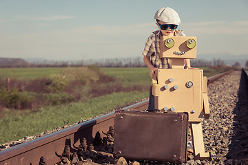 Image showing Happy little boy and robot walking with suitcase on the railway 