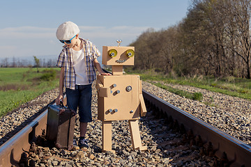 Image showing Happy little boy and robot walking with suitcase on the railway 