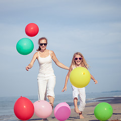Image showing Mother and daughter playing with balloons on the beach at the da