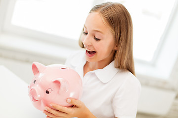 Image showing happy girl with piggy bank at home
