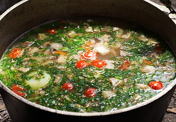 Image showing Freshly cooked hot soup in sooty cauldron on camp fire