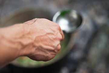 Image showing Man\'s hand with metal ladle (spoon) and soup in cauldron at back