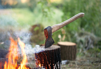 Image showing Axe in tree stump and campfire with smoke