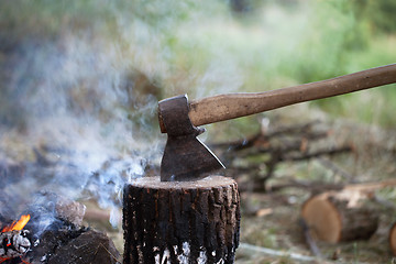 Image showing Axe in tree stump and campfire with smoke