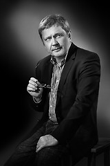 Image showing Handsome pensive mature businessman in formal suit is looking while sitting on chair, on gray background