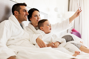 Image showing happy family with smartphone in bed at hotel room