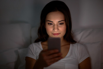 Image showing happy young woman with smartphone in bed at night