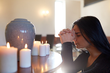 Image showing sad woman with funerary urn praying at church