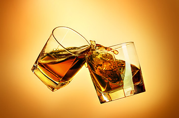 Image showing Two whiskey glasses clinking together on brown