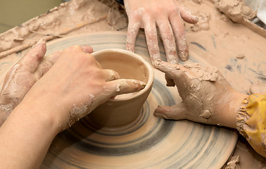 Image showing Beginner and teacher hands in clay at process of making crockery