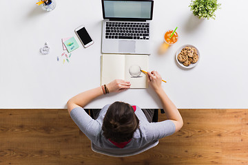 Image showing woman with laptop drawing in notebook at office