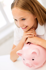 Image showing happy girl with piggy bank at home