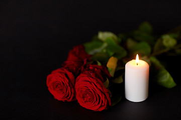 Image showing red roses and burning candle over black background