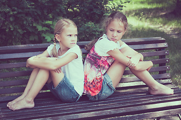 Image showing two sad sister sitting on the bench in park 